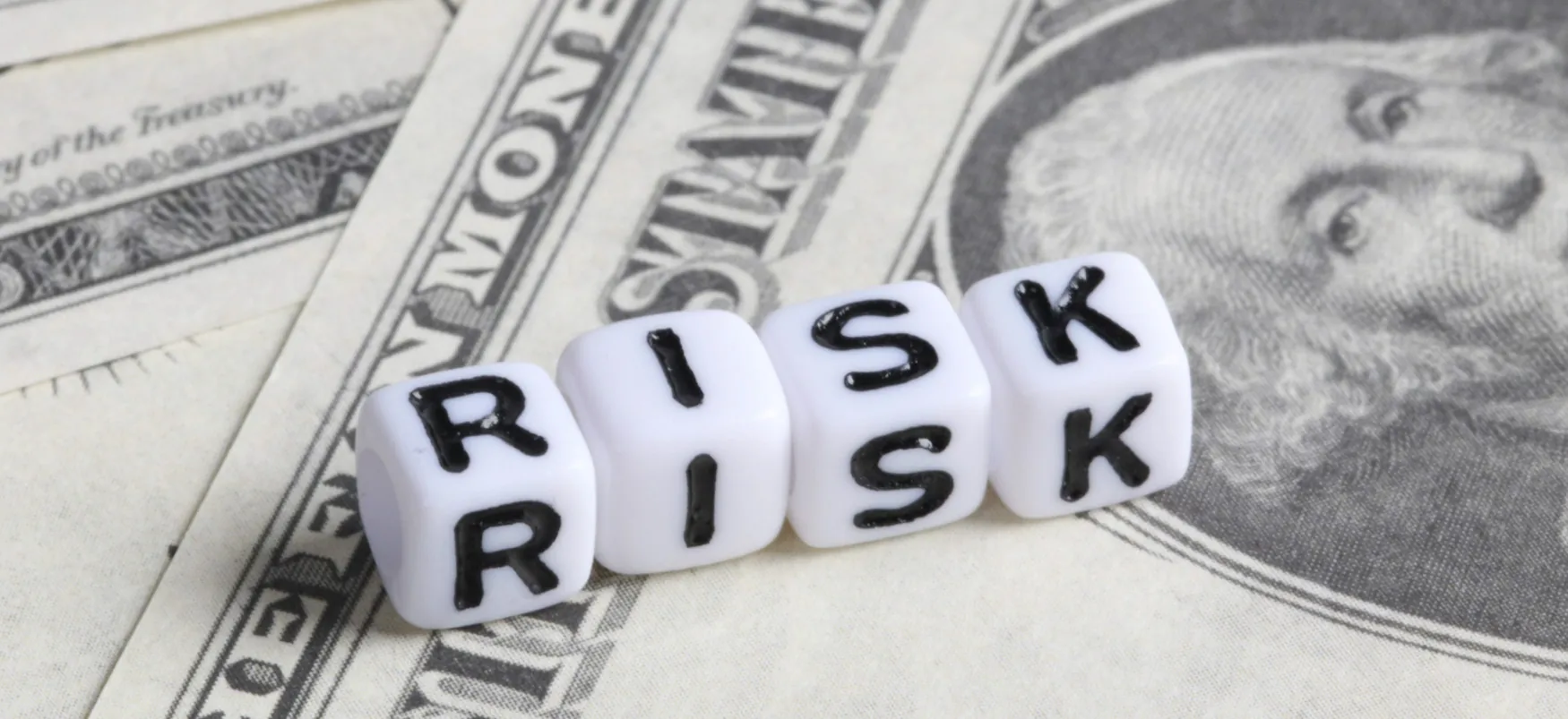 Lettered dice spell out the word risk on top of dollar bills.