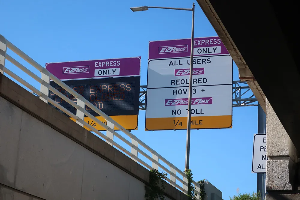 Several large E Z Pass road signs in a cluster. They indicate that the lane is E Z Pass Express Only. One says “All Users E Z Pass Required,” while another indicates that H O V lane requires no toll.