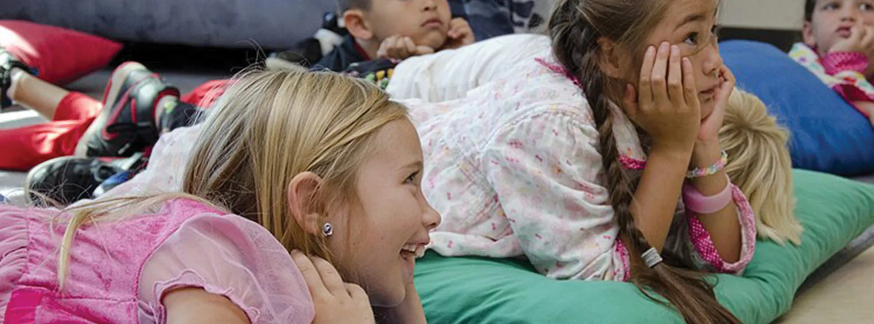 Photo of group of young children laying stomach down on pillows and looking up.