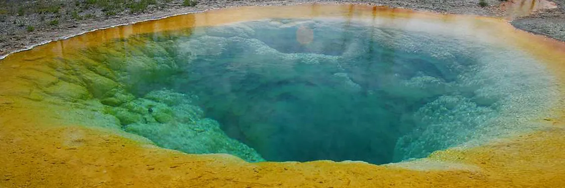 The photo shows a hot spring with a vivid blue color in the middle and a golden color around the edge.