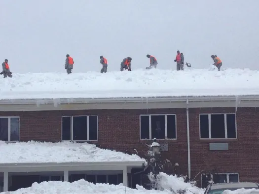 An image of several people standing on top of the roof of a brick building. The roof is covered in snow.