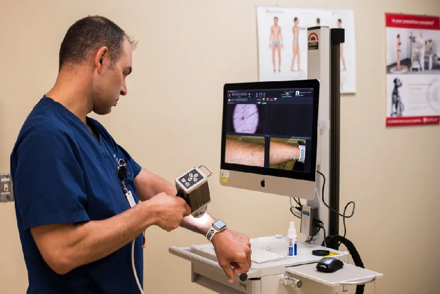 Photo of healthcare worker using a scanner to look at images on their arm. Images are displayed on a computer screen attached to the scanner.