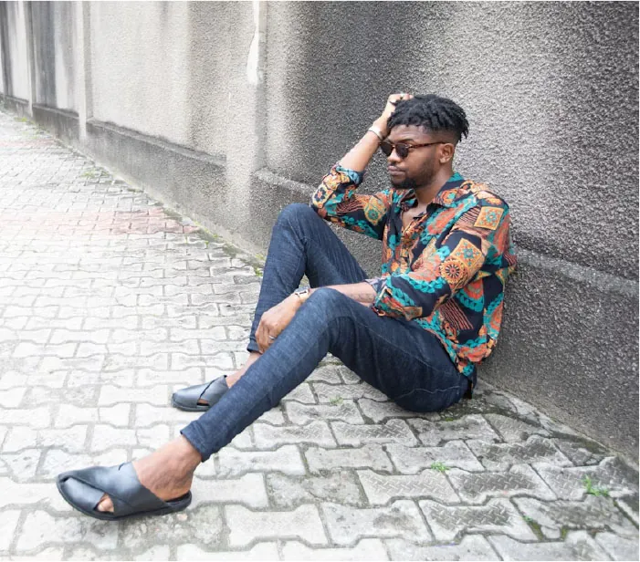 Photo of individual sitting on the ground, leaning up against a wall, with their hand holding up their head.