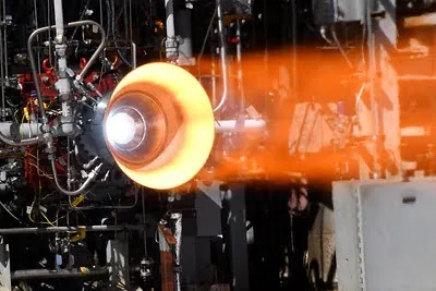 The exhaust cone of a rocket engine emits hot gas and light, inside what appears to be a lab or similar facility.