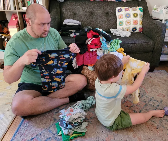 Photo of child and adult folding clothes while sitting on the floor.
