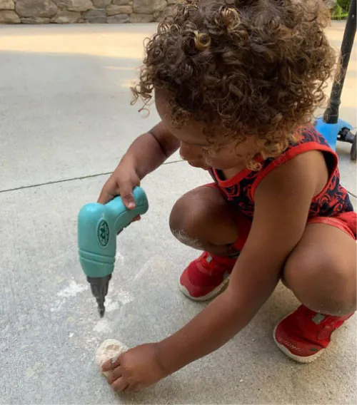 Image of a small child squatting and playing with a toy drill.