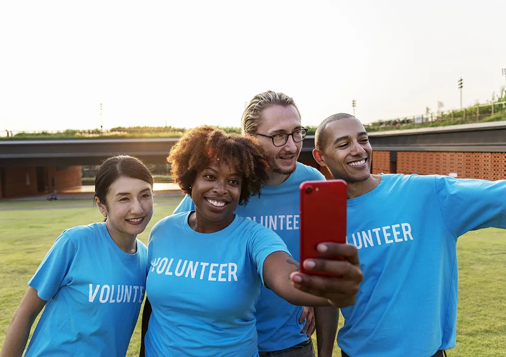 A diverse group of employees wearing volunteer shirts take a photo of themselves with a phone’s camera.