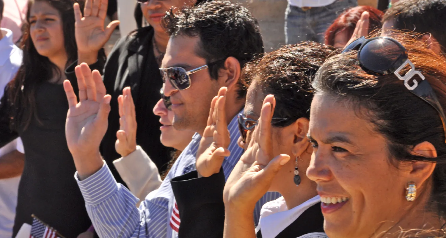 A group of people raise their right hands as they take the Oath of Allegiance during a naturalization ceremony.