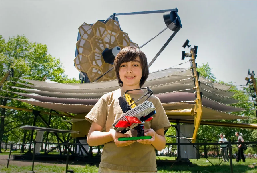 Photo of child holding a small model in front of the same, large art piece.