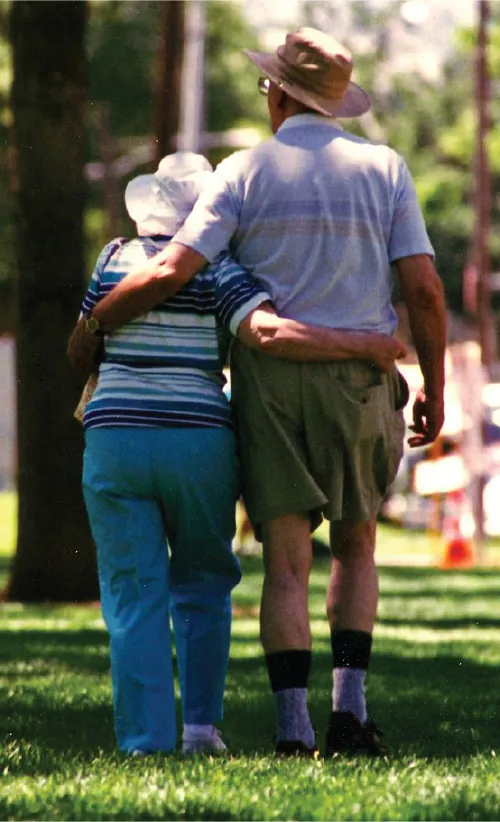 An older couple walks through a park.