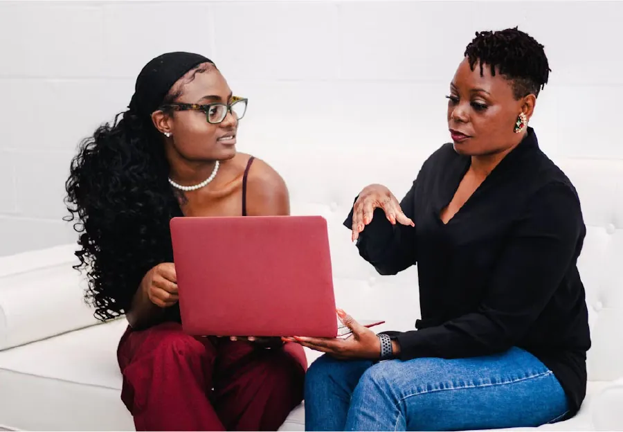 Photo of a young adult speaking with an adult while holding a laptop between them.