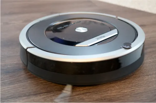 A small black and silver circular robot vacuums a floor.