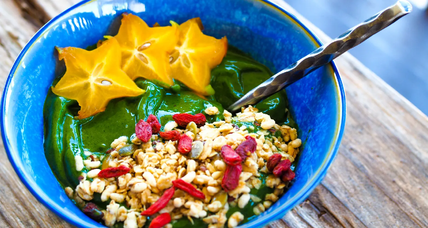 A bowl contains starfruit and whole grains on top of green spirulina.