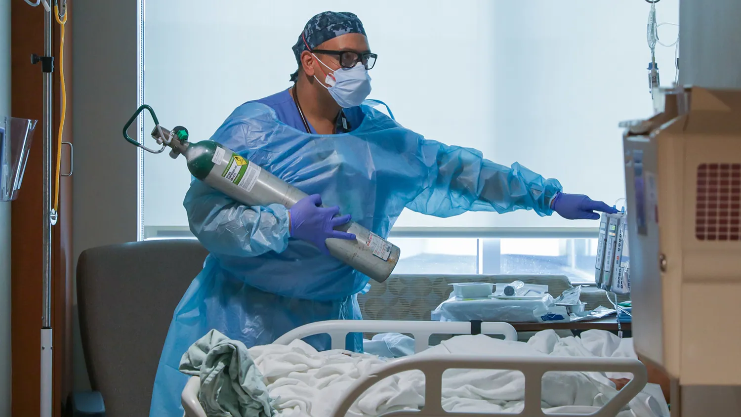 A nurse carries a portable oxygen tank in a hospital room.