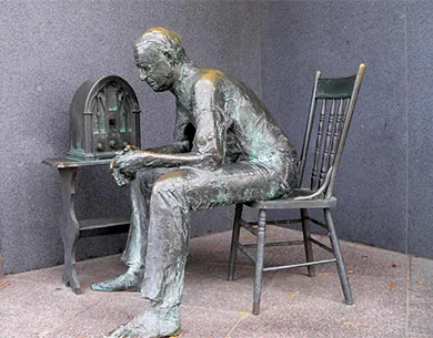A sculpture shows a man sitting in a chair beside a radio.