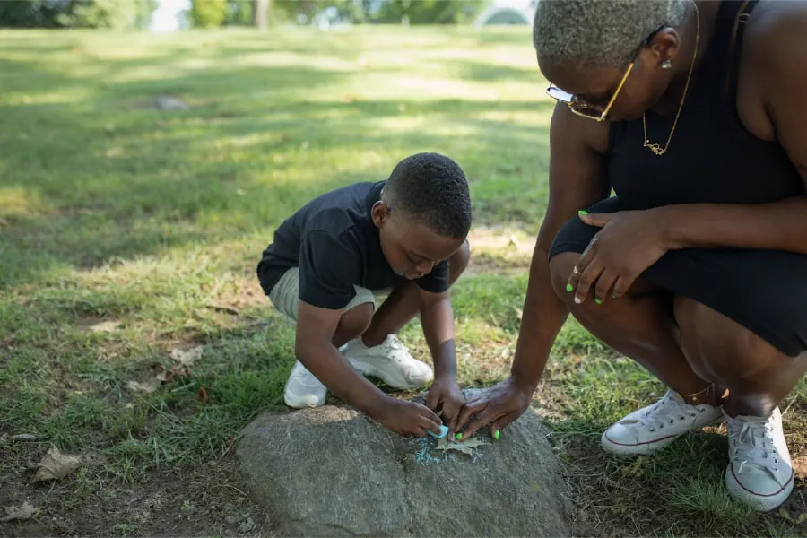 Photo of a grandparent and grandchild coloring with chalk outside.
