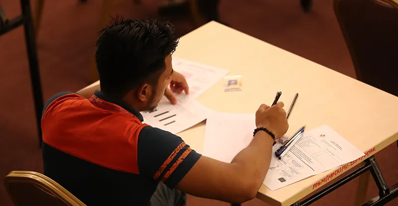A person holding a pen sits at a desk with a set of papers.