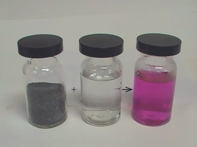 Three glass containers with lids are shown in a photo. A plus sign is drawn between the first two containers and a right-facing arrow is drawn between the second and third containers. The left container holds a black granular solid while the center container holds a clear, colorless liquid. The right container holds a clear, pink liquid.