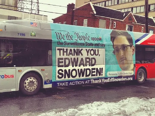An ad on the side of a bus featuring a photo of Edward Snowden. The text says “We the people oppose the Surveillance State and say ‘Thank you, Edward Snowden!’”