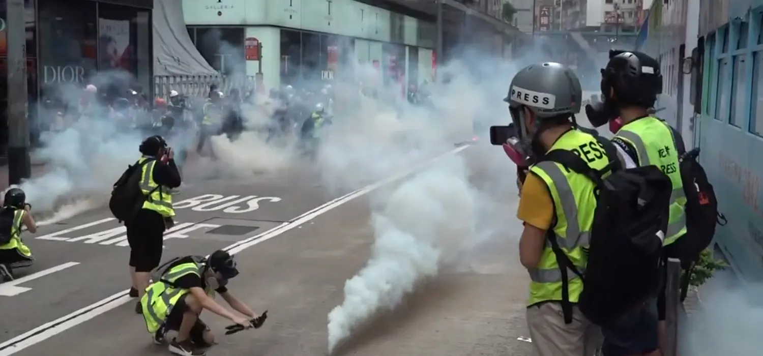 A photo shows tear gas being deployed on the streets of a city and people from press taking pictures of the street.