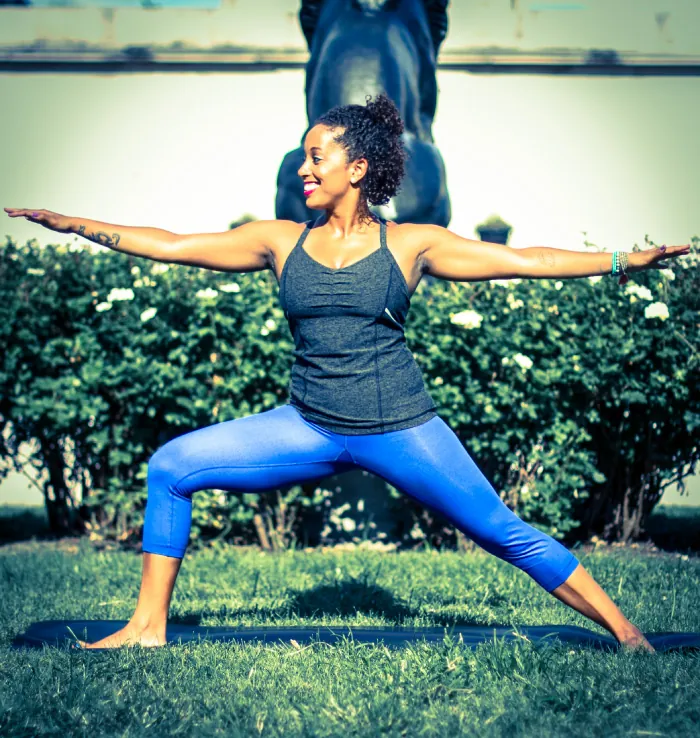 Photo of woman doing yoga outside on a mat spread out on a grassy area.