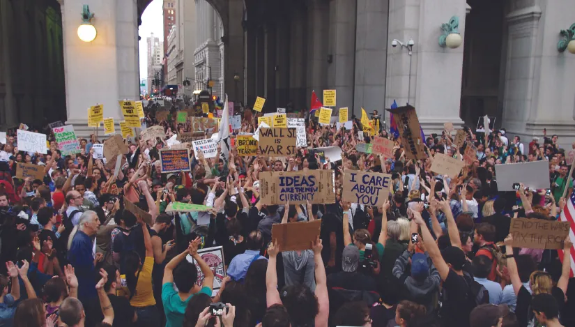 An image of a large crowd of people, several of whom are holding signs.