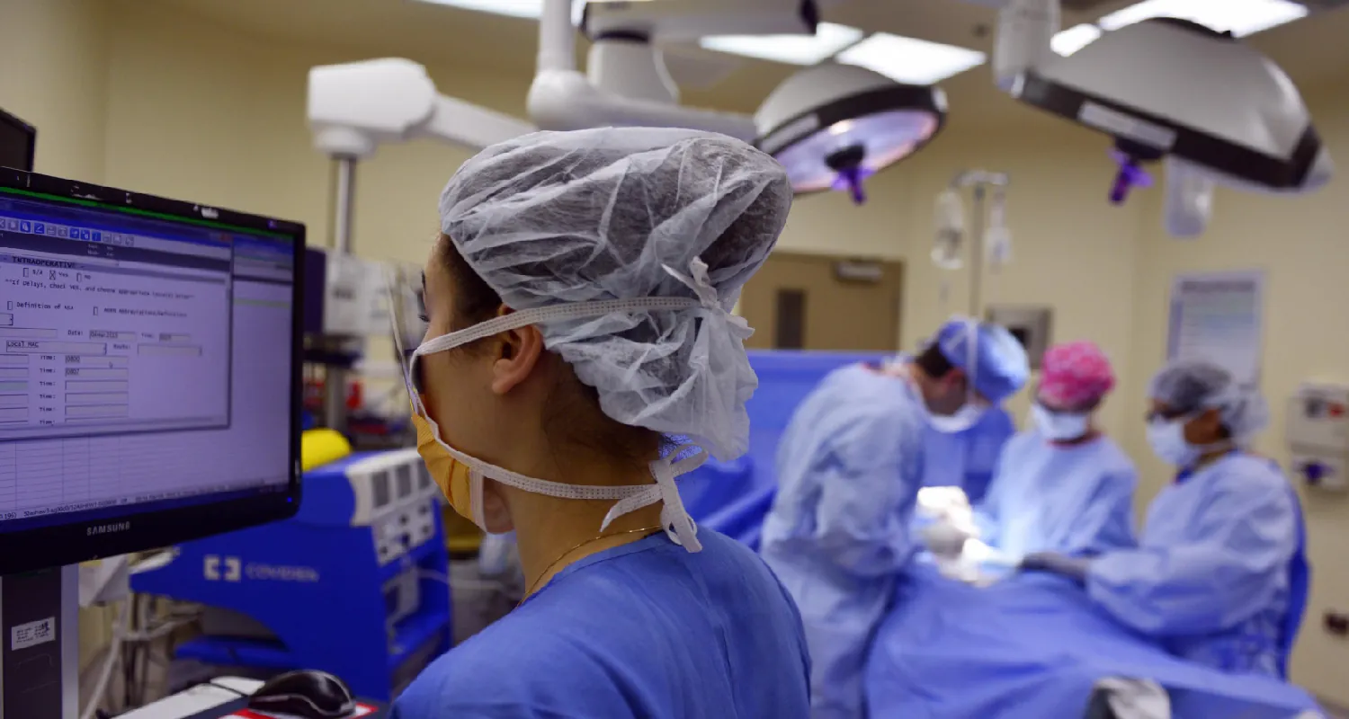 Photo of medical staff performing surgery while one staff person looks at a computer screen off to the side.