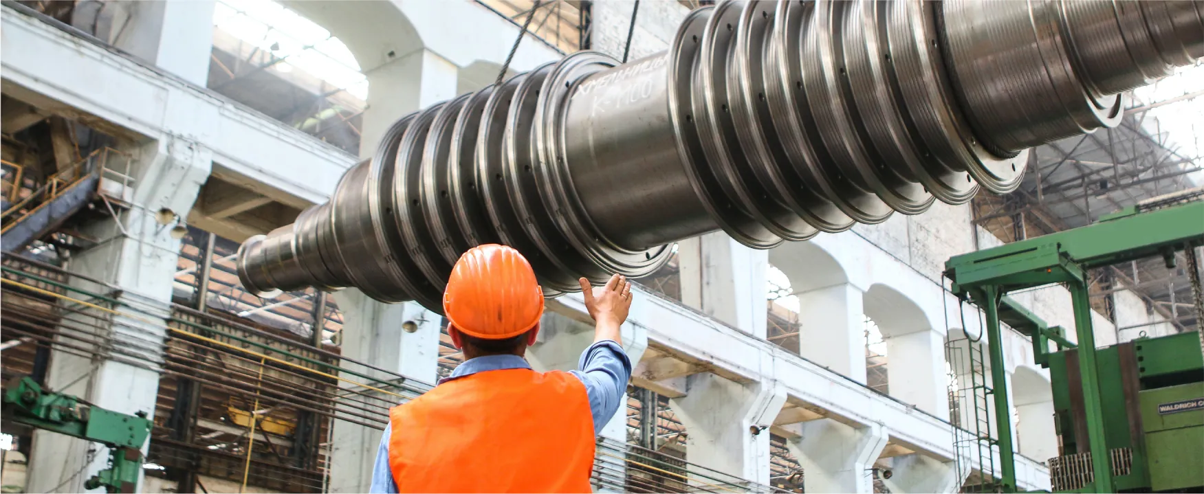 A person stands next to machinery in an industrial manufacturing facility.