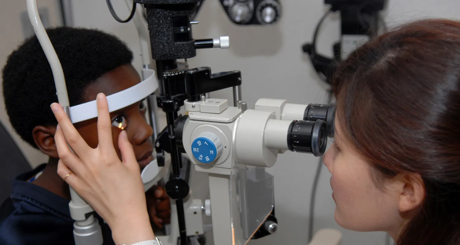 A color photograph shows a medical professional using a machine to examine the eyes of a young patient.