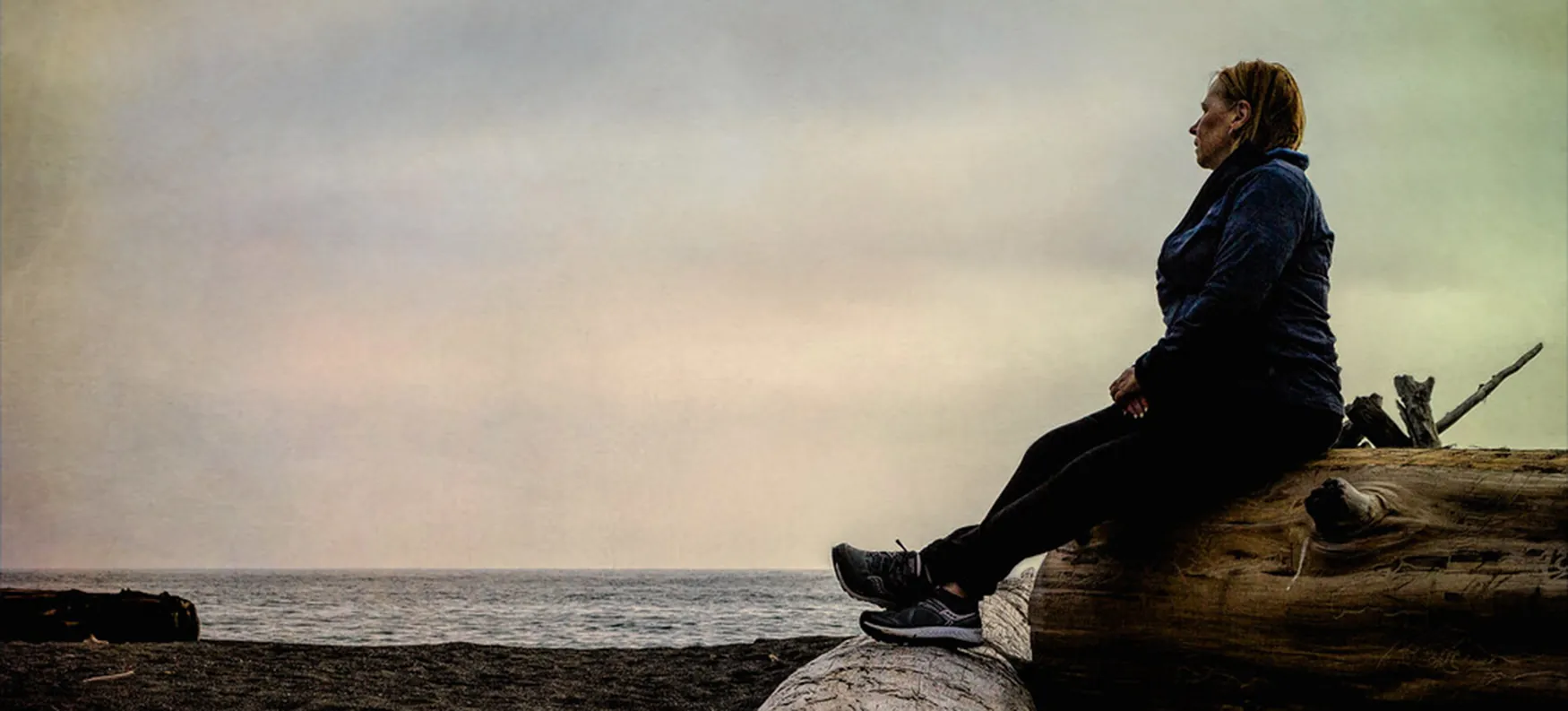 An older person sits on a beach and looks to the water.