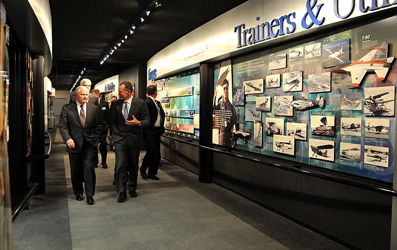 A group of businesspeople walk in a hallway, passing a photo essay about changing aircraft design.