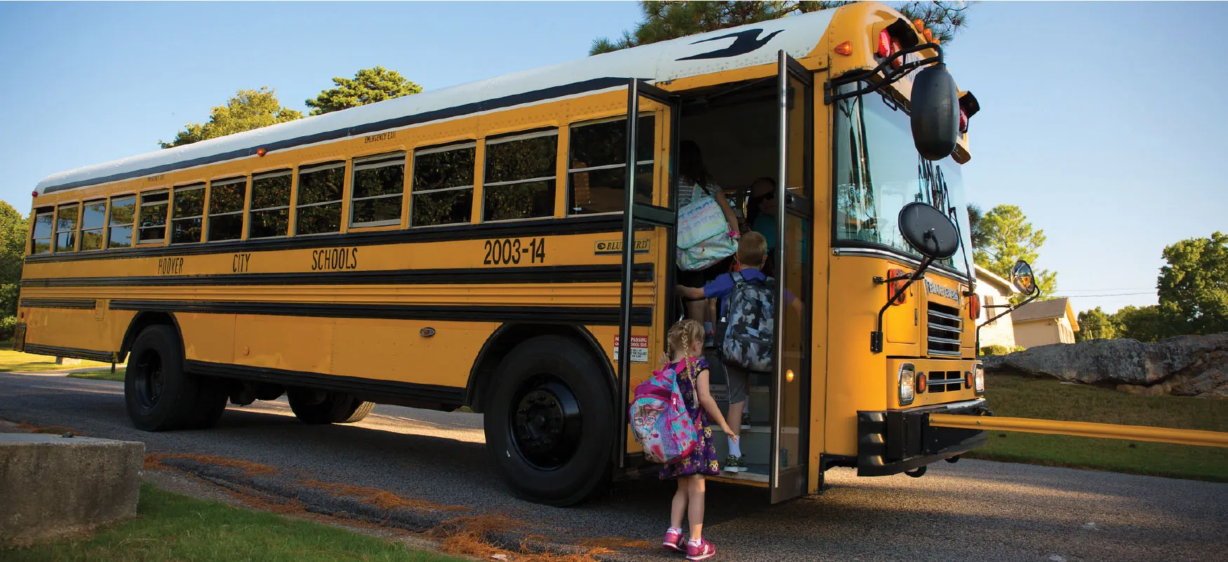 Photo of young children with backpacks getting onto a yellow school bus.