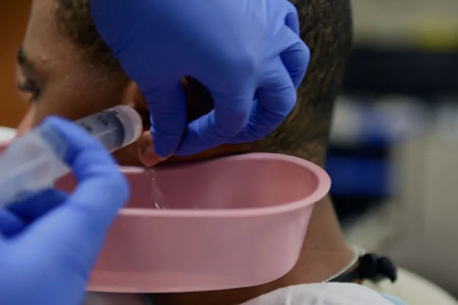 A photo of a provider using a syringe of liquid to irrigate a patient’s ear.