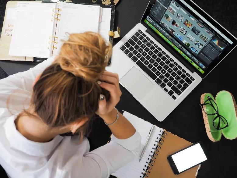 A photo shows the overhead view of a stressed female student sitting at a table, with notebooks, a smartphone, spectacles, and a laptop around her.