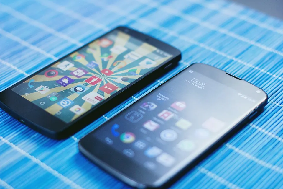 Two smartphones lying side by side on a blue-striped surface, with their screens displaying colorful app icons and home screens.