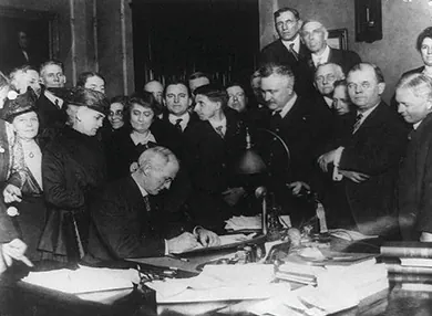 A photograph depicts Governor James P. Goodrich signing a bill, surrounded by a large group of men and women.