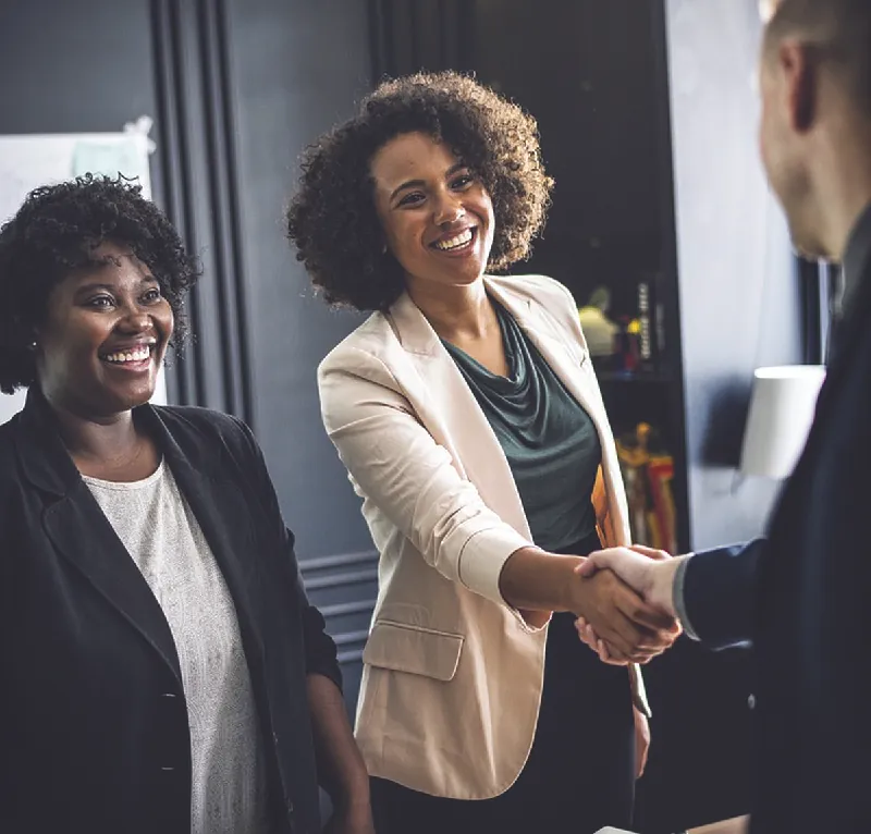 Photo of two women with a man; one of the women is shaking his hand.