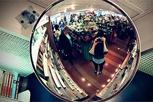 The image shows a woman taking a picture in front of a convex mirror.