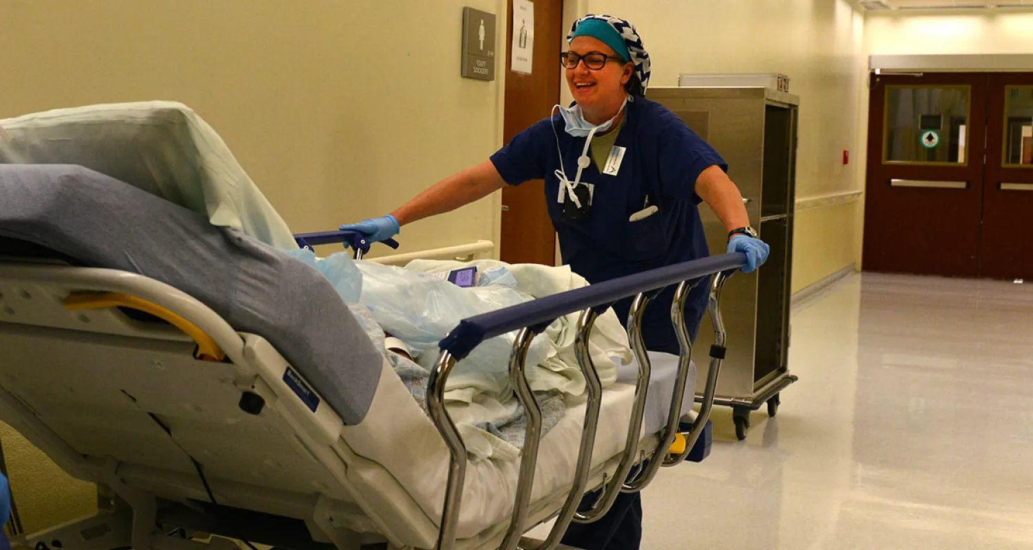 Photo of medical personnel wheeling medical bed down a hospital hall.