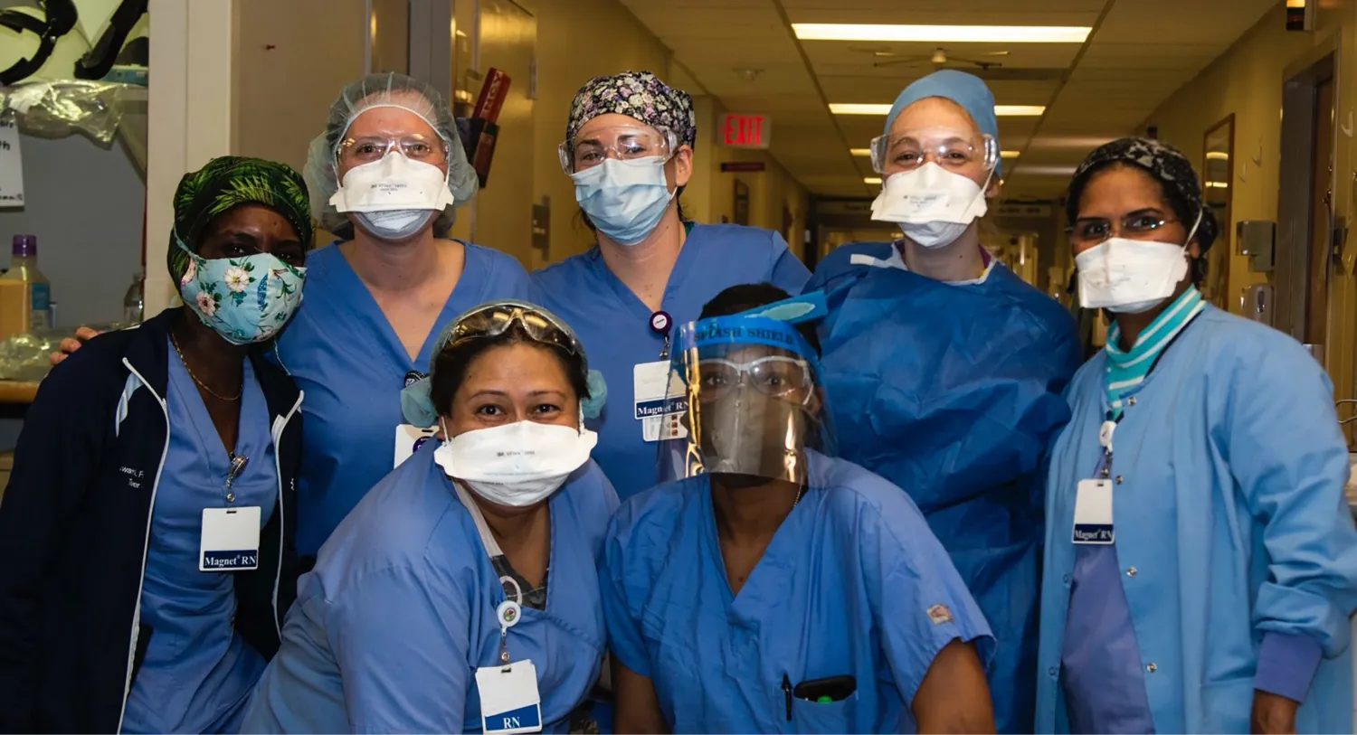 A color photograph shows several nurses wearing masks and/or face shields in a hospital hallway.
