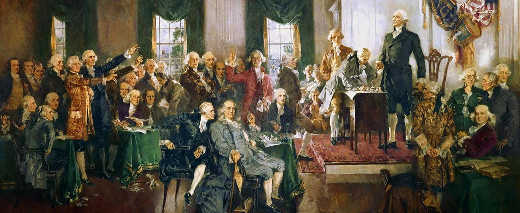 The image displays Howard Chandler Christy’s painting, titled Signing of the Constitution.  The painting depicts forty people seated or standing around a room in what is now known as Independence Hall.  Featured are George Washington, Benjamin Franklin, Alexander Hamilton, and James Madison.  In the moment captured by the artist, delegate Richard Spaight of North Carolina signs the Constitution.