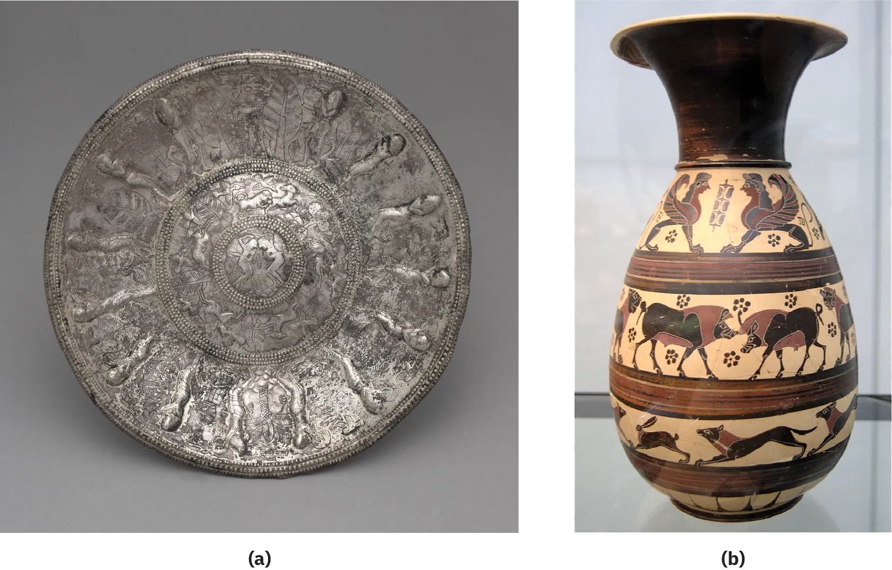 Two images of a bowl and jug are shown. The (a) faded silver bowl is round and shown standing up on a gray background. The outer perimeter is not smooth and shows small circles all around the bowl. Repetitive designs of leaves and people run on the outer circle. The next inner circle repeats designs of animals, leaves, and fowl. The final inner circle shows two figures facing each other. Small circles of tiny dots separate the three rings. (b) An image of a jug is shown on a flat gray surface with a gray background. The jug is fluted at the top with a short black neck. The bottom of the jug is pear shaped and has four rows of scenes depicted on a beige background and six-petaled black flowers strewn in the first two rows. Brown, red, and black stripes separate the rows of scenes. The top row shows two winged creatures with four paws each and a human looking head with long curly black hair. The wings show multi-colored feathers in black and brown and a long thin tail is seen at their hind ends. The next row shows large black animals with four legs and brown manes and underbellies with long snouts and large ears – two in the middle facing each other and two more at each end only showing their raised heads. The next row shows two long, thin, black animals with four paws, tails, and brown necks facing to the left and one with long ears and a bit smaller in front of them at the left. The last row shows a beige background with black lines.