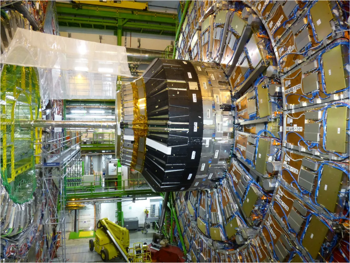 A photo of a portion of the Large Hadron Collider. It features a very large circular assembly of devices connected with cables. 