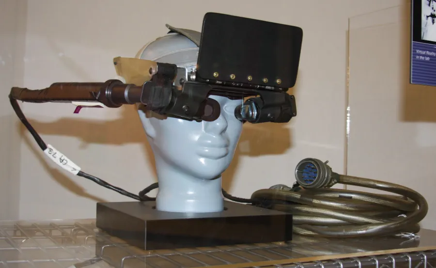 Photo of first VR prototype on a fake head. A large screen is visible over the eyes with long tubes coming off right side of unit and leading to a long cord.