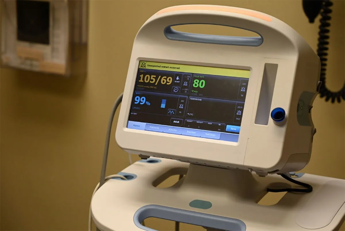 A medical vital signs monitor displays blood pressure 105/69, pulse rate 80, and SpO2 99%, with an 'Unexpected restart occurred' message on the screen.