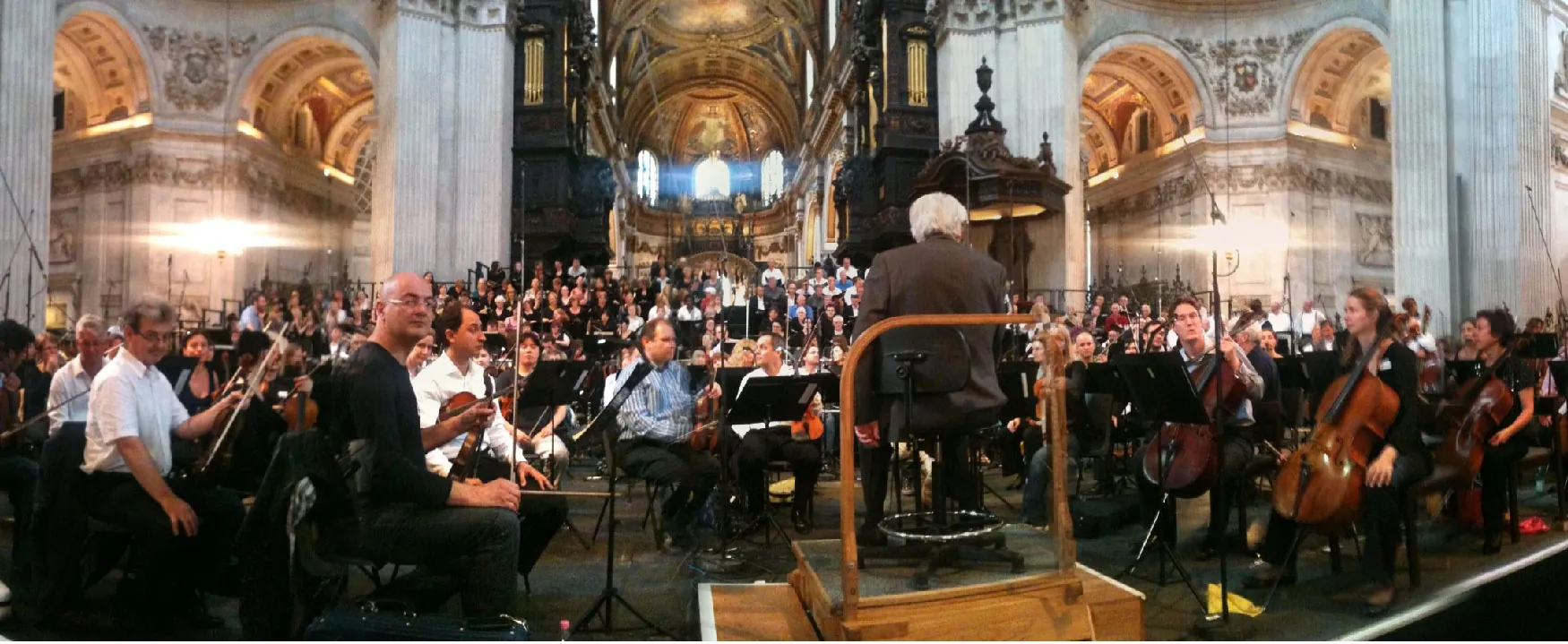A grand orchestra and choir fill a magnificent cathedral with music, guided by their conductor. The ornate architecture and towering pillars create an awe-inspiring setting for the performance.