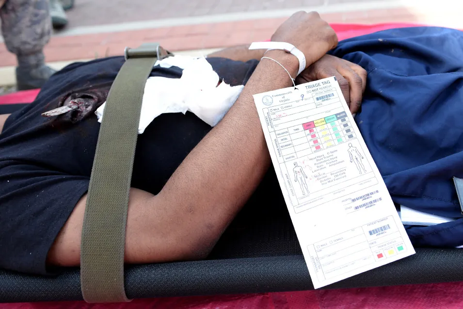A color photograph shows a patient lying and strapped to a stretcher with a triage tag on his wrist.