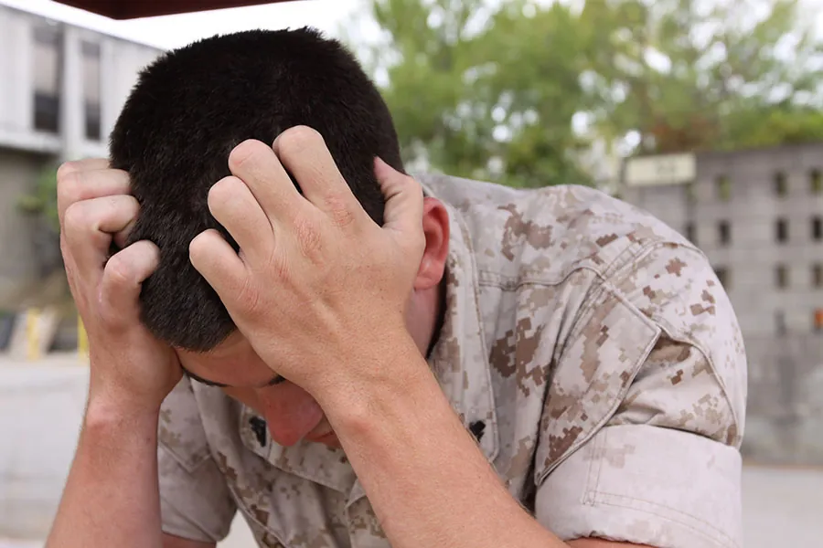 Man with his head bent and his hands with fingers bent inward placed on his head in apparent distress.