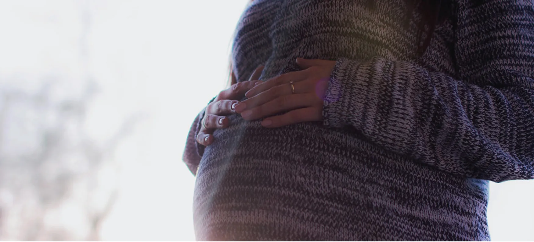 Photo of person resting their hands on their pregnant belly.