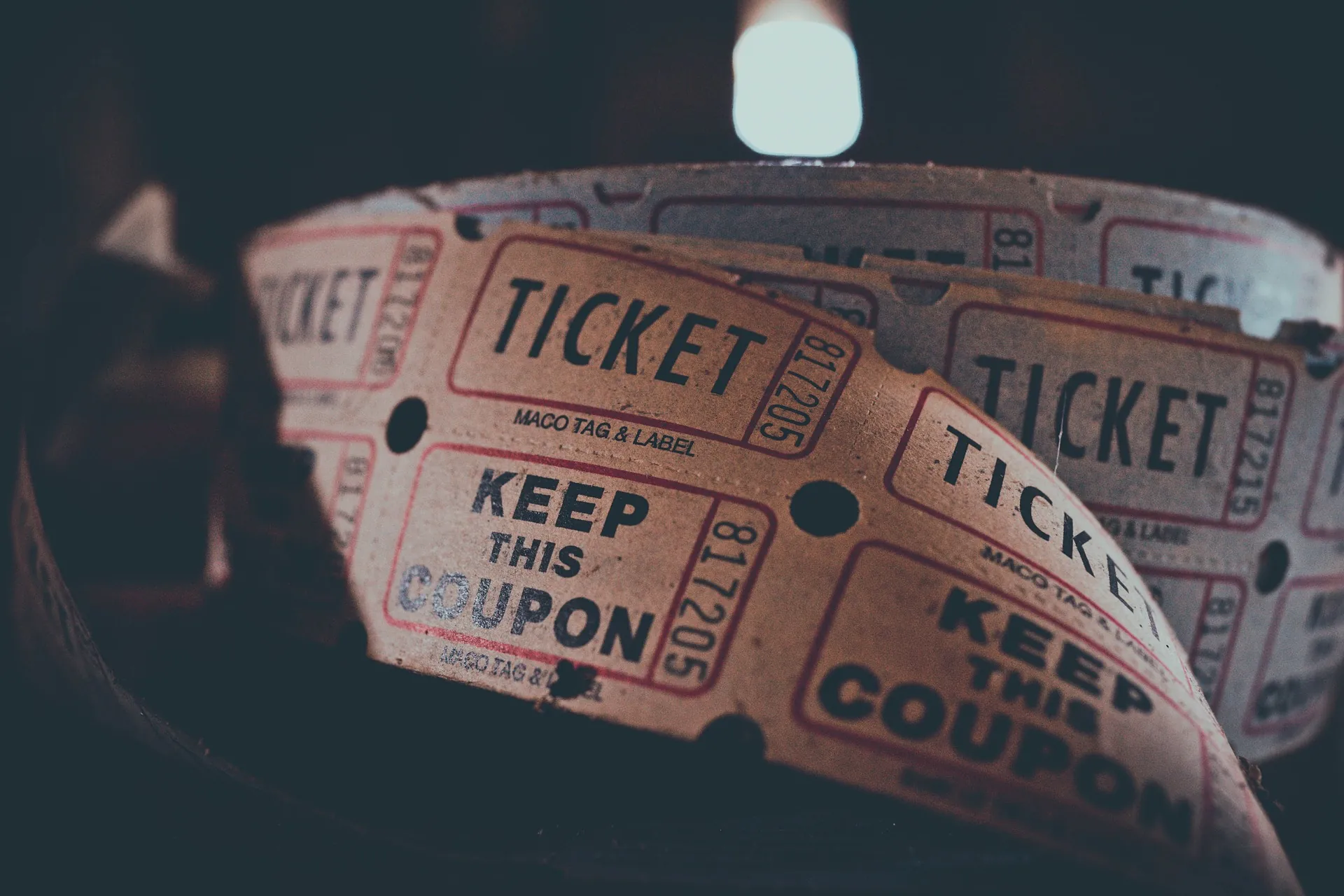 A close-up of a roll of vintage-style raffle or event tickets with TICKET and KEEP THIS COUPON printed on them, illuminated by soft, warm light.